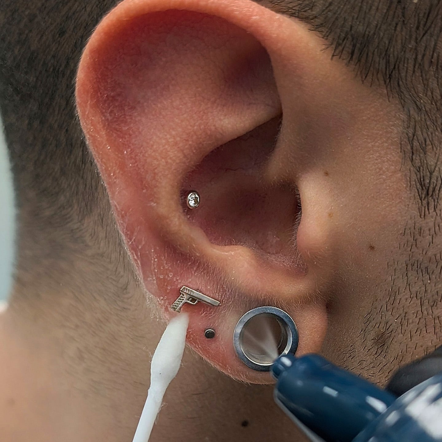 Place the cotton bud next to your piercing, and spray your saline solution directly on to that area, saturating the cotton bud and your piercing nicely.